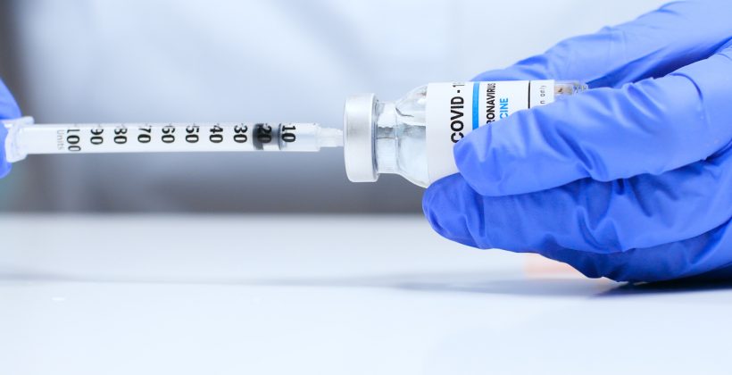 hands in medical gloves holding COVID vaccine dose and syringe